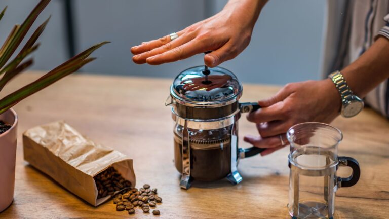 French press coffee brewing on a wooden table with coffee beans nearby